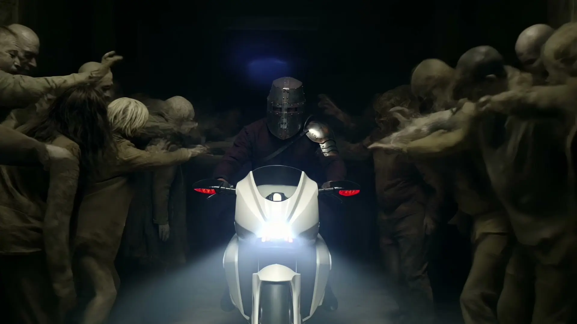 The King rides a white motorcycle through a corridor packed with zombies, a frame from Burn It Down